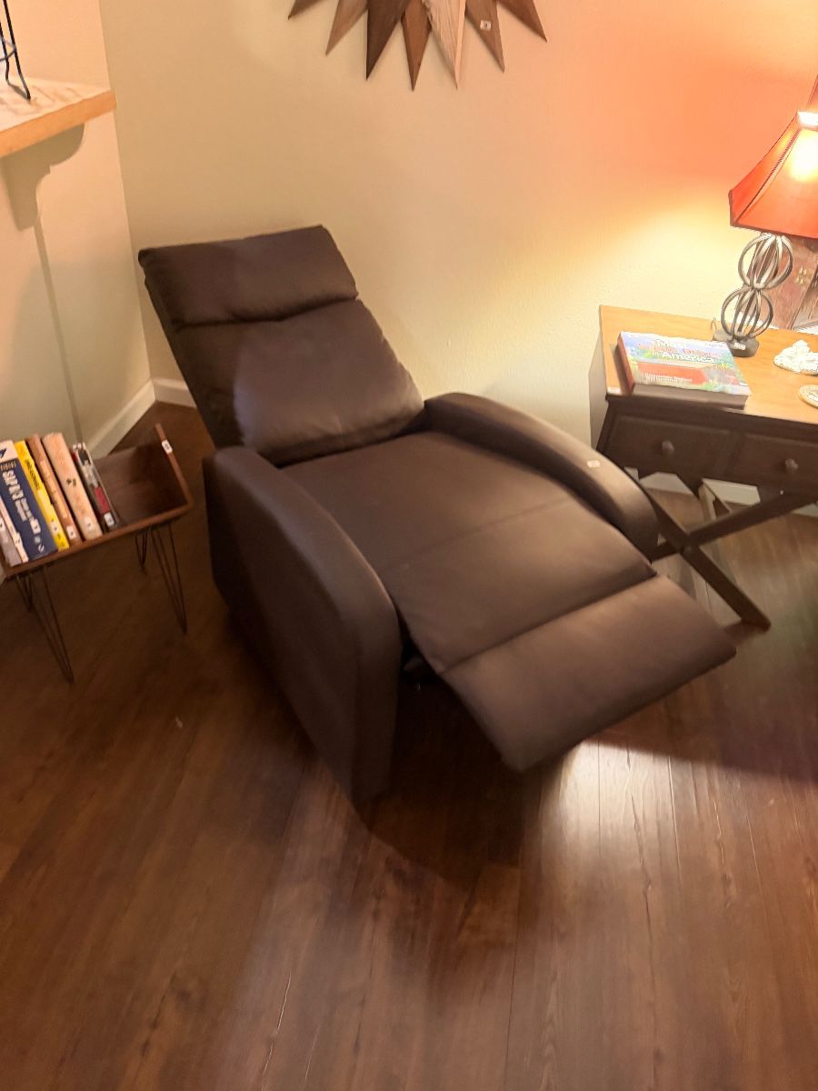 Brown leather recliner beside a bookshelf and lamp table