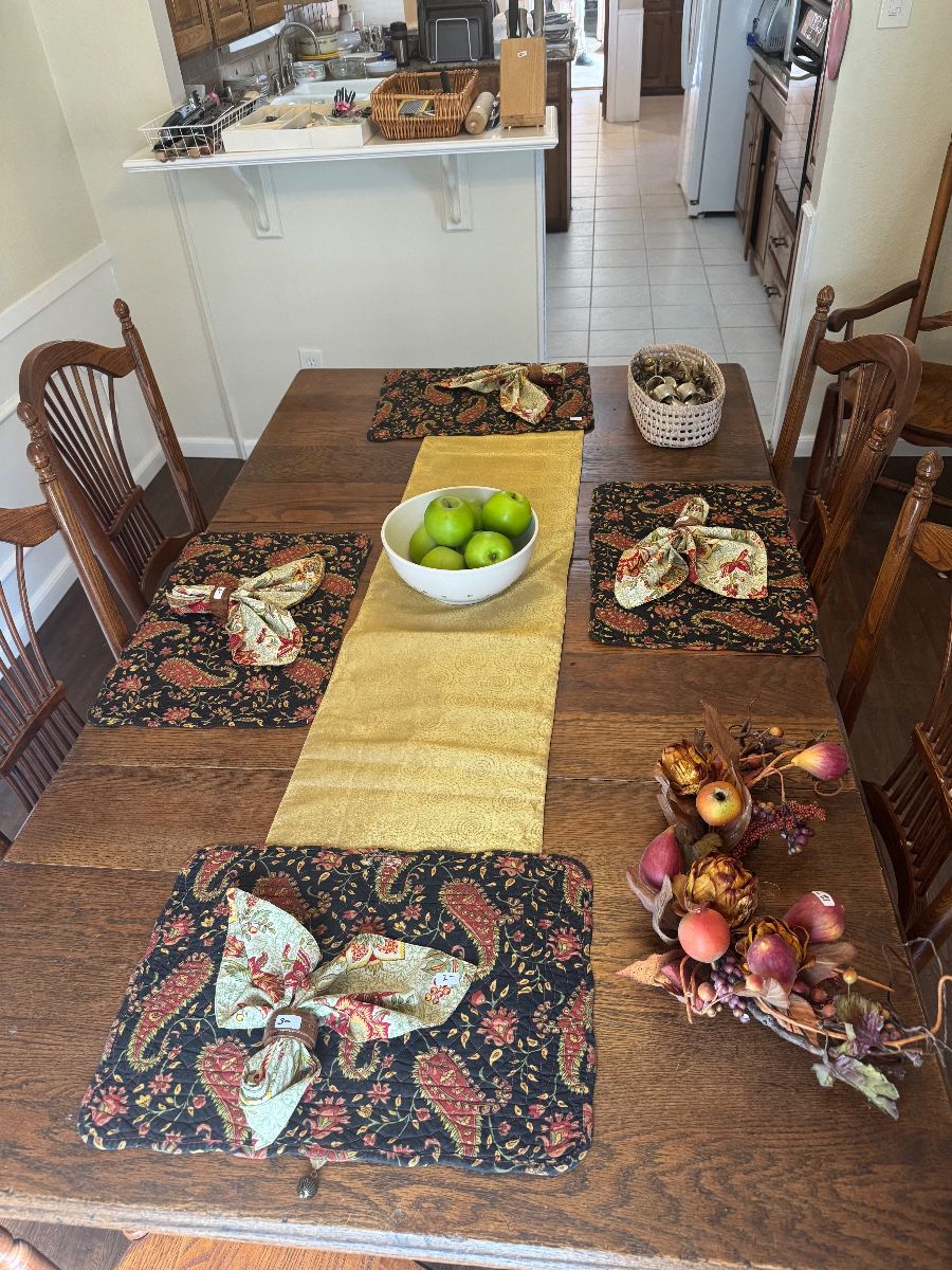 Farmhouse dining table set with paisley placemats and a gold runner