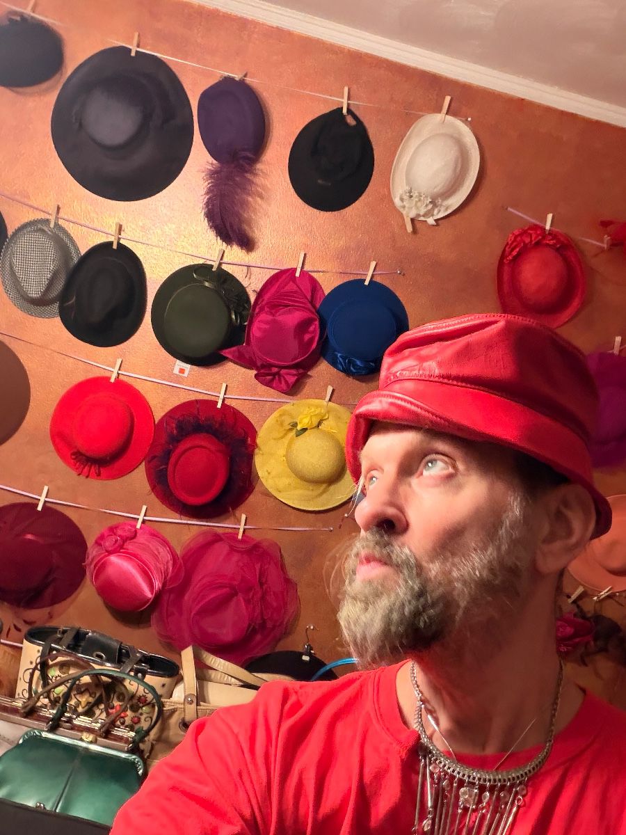 James Major of James Major Estate Sales trying on a red hat in front of the hat collection