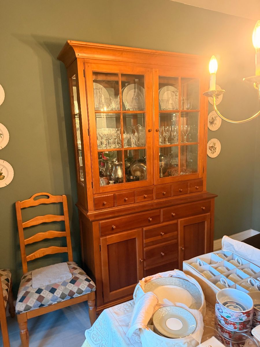 Pine china hutch filled with glassware beside a ladder-back dining chair