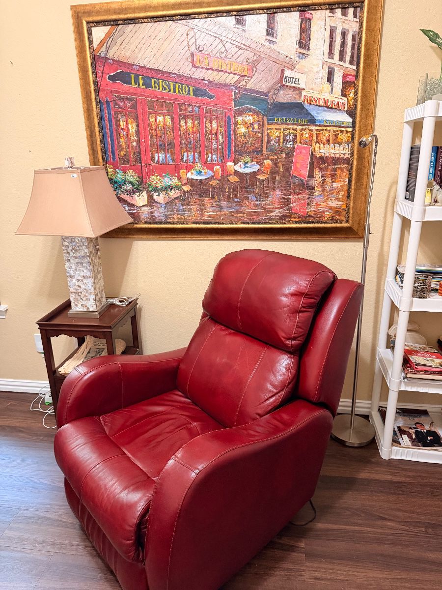 Red leather recliner below a framed street scene painting