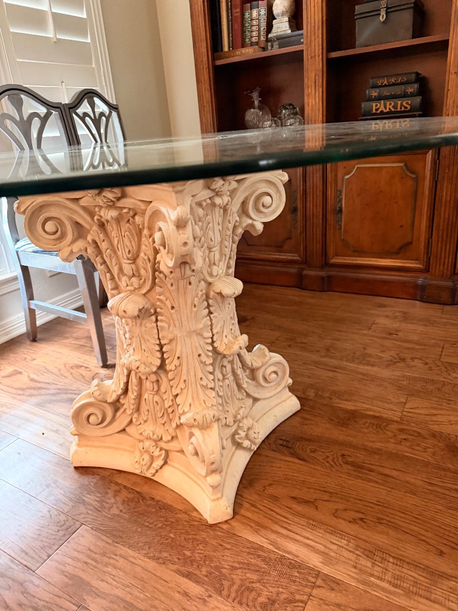 Round glass dining table on a carved pedestal base