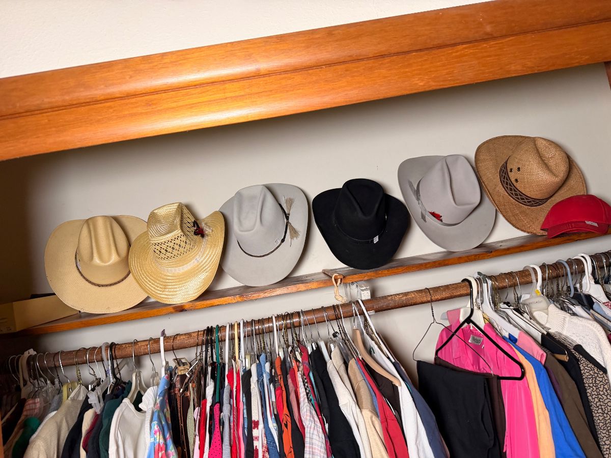 Shelf of cowboy hats above a closet of clothing