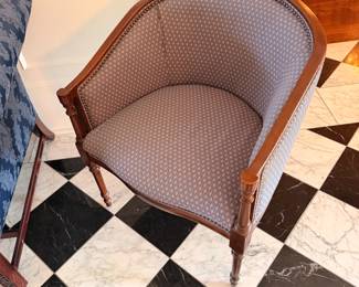 Upholstered barrel back chair on a black and white checkerboard marble floor