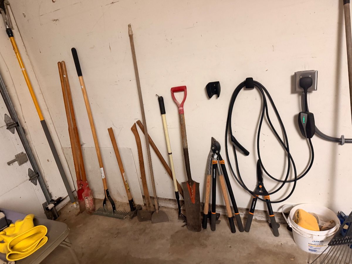 Wall of shovels, rakes, loppers and garden hoses in the garage